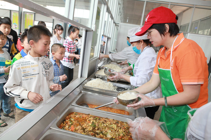 河南三门峡志愿者王鲜芳正在帮助厨师盛饭。